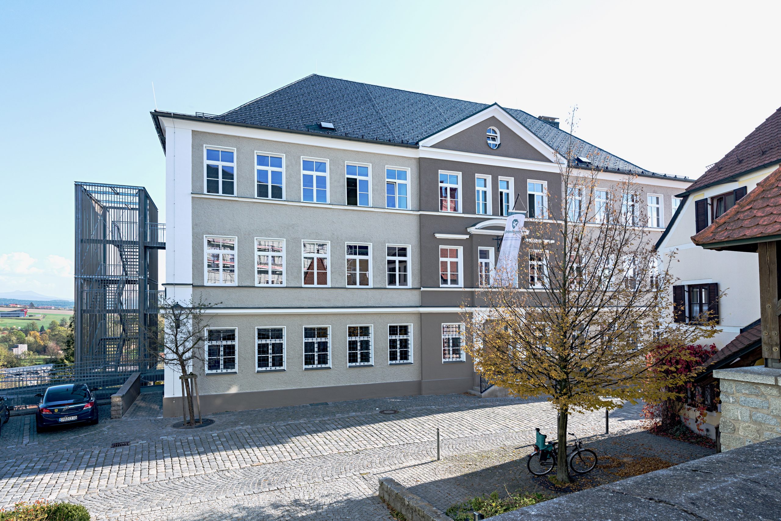 Außenaufnahme der Eingangsfassade der Fachakademie für Sozialpädagogik Furth im Wald mit gegliederter Putzfassade und zusätzlichem Treppenturm in reduzierter Gestaltung.