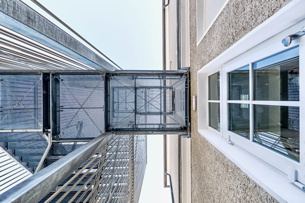 Detailfoto des Treppenturms der Fachakademie für Sozialpädagogik Furth im Wald, von unten nach oben fotografiert, mit sichtbarem Abstand zum denkmalgeschützten Bestandsgebäude.