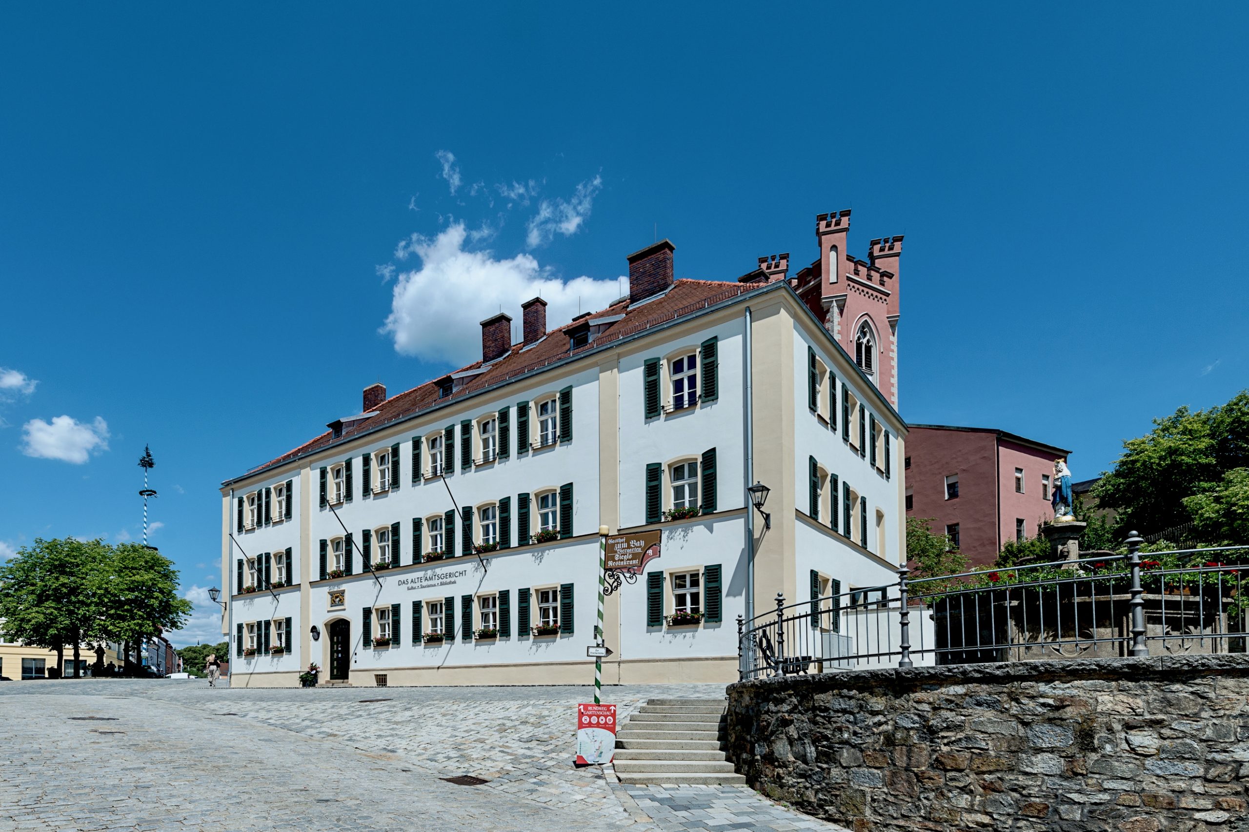 Außenaufnahme des Alten Amtsgerichts Furth im Wald von Südwesten mit Hauptfassade, Eingangsbereich und dem Stadtturm im Hintergrund.