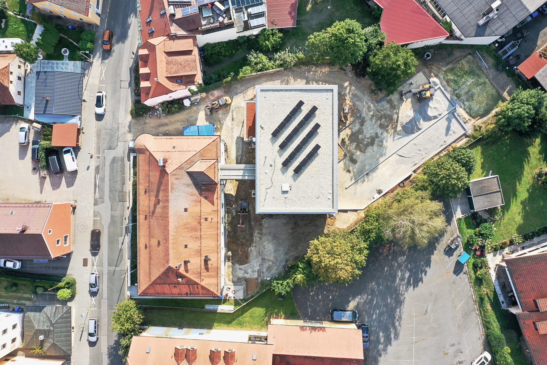 Drohnenaufnahme aus der Vogelperspektive des Finanzamts Waldmünchen, Außenstelle des Finanzamts Erlangen, mit Neubau in Holz-Hybridbauweise, verglastem Verbindungsgang und denkmalgeschütztem Altbau; Außenanlagen im Bau, Nachverdichtung in zweiter Reihe erkennbar.
