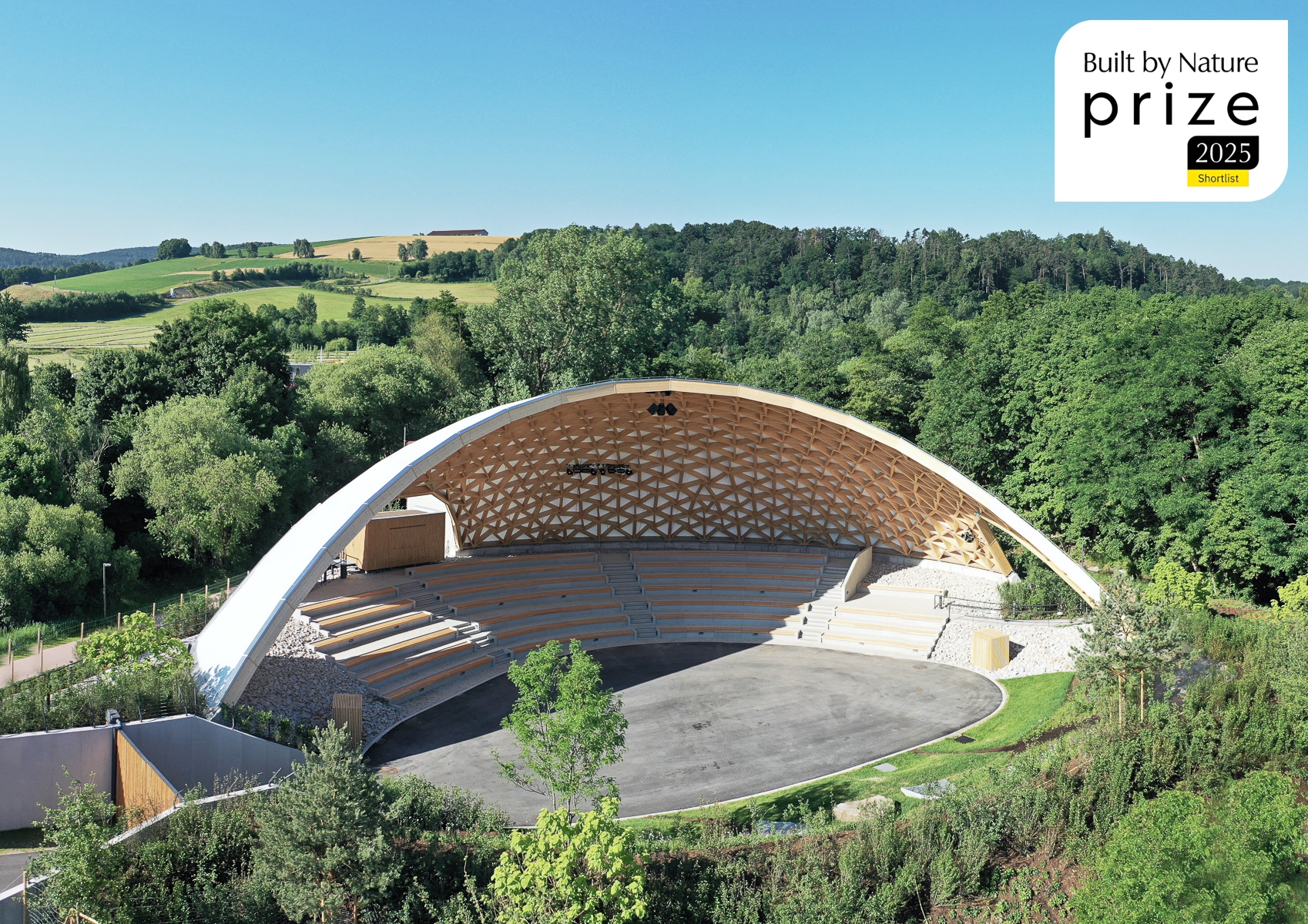 Drohnenaufnahme der Park-Arena Furth im Wald von Norden, eingebettet in das umgebende Grün kurz vor der Eröffnung der Landesgartenschau mit Built by Nature Prize Shortlist 2025 Logo.