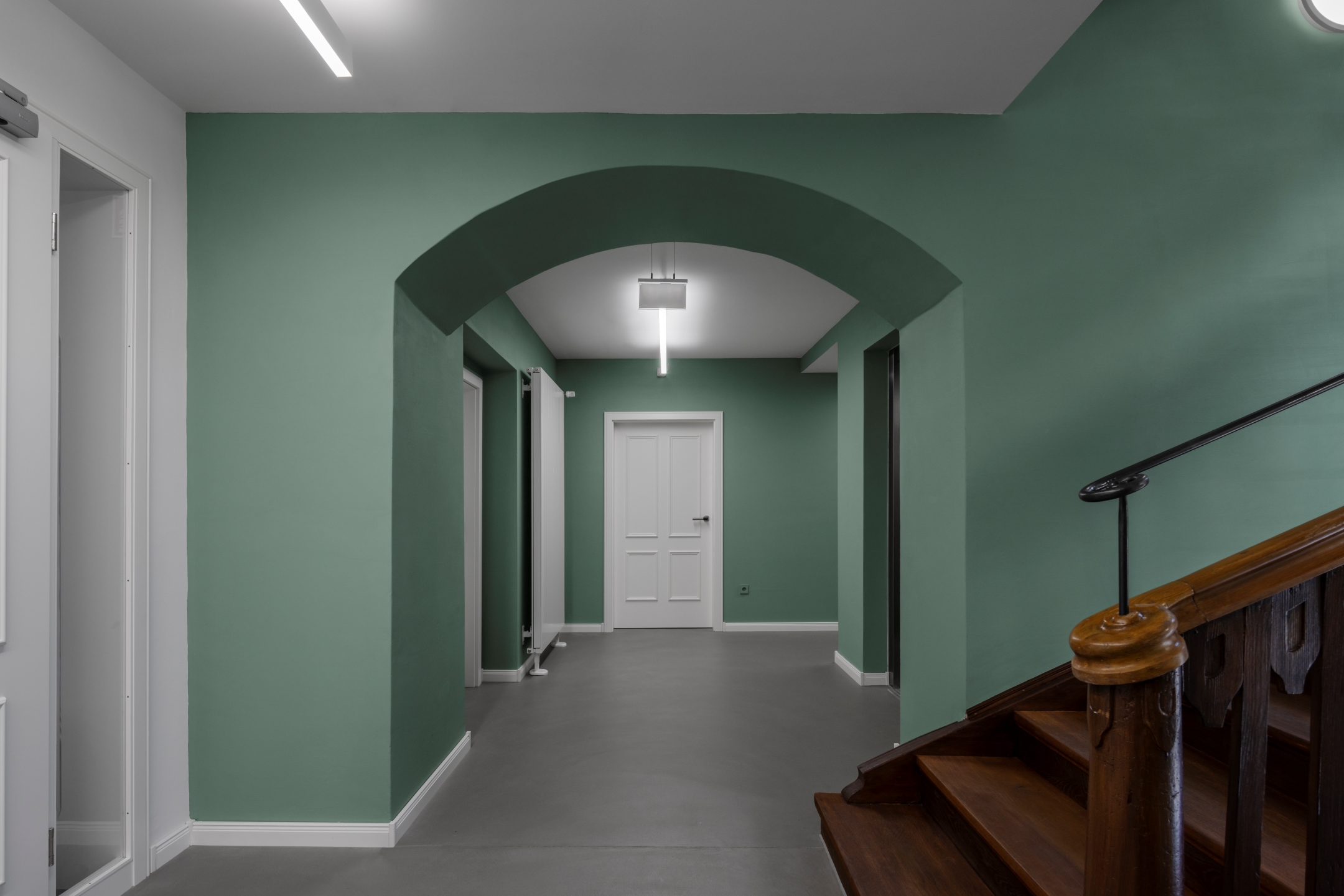 Treppenraum im Erdgeschoss des Alten Amtsgerichts Furth im Wald mit restaurierter historischer Treppe, Wänden in Grünton und neuen weißen Türen.