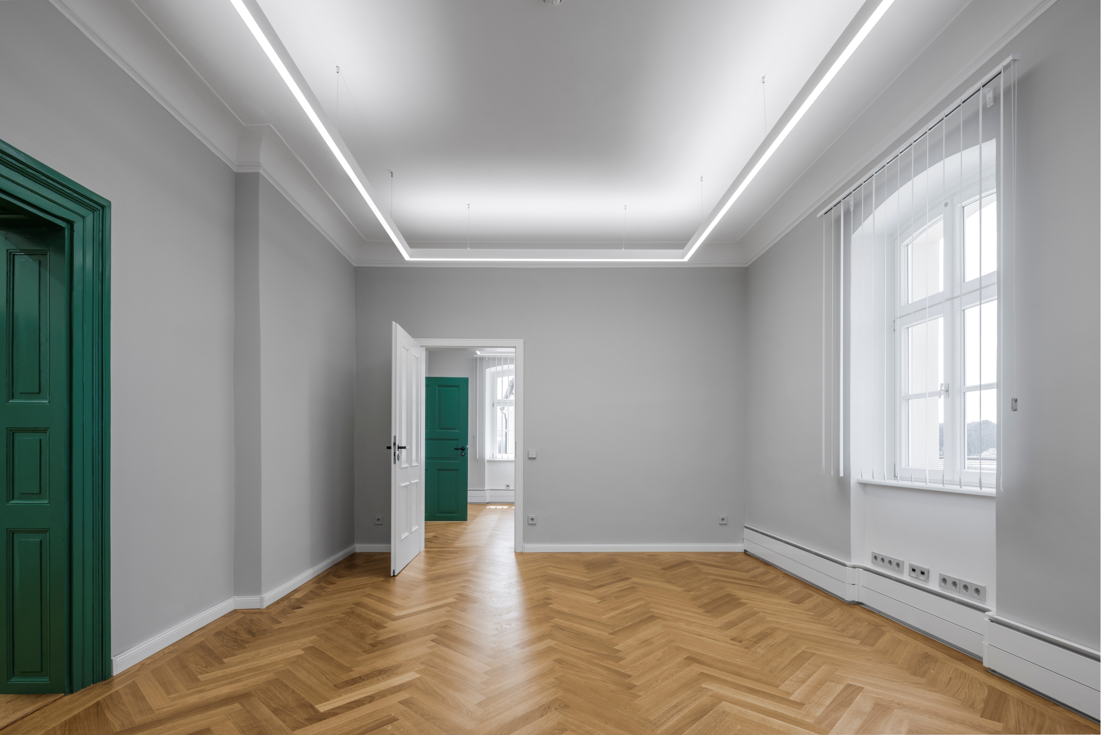 Raumkombination im 2. Obergeschoss des Alten Amtsgerichts Furth im Wald mit Eiche-Parkett, grauen Wänden, weißen Stuckdecken, historischen dunkelgrünen Türen und einer neuen weißen Tür.
