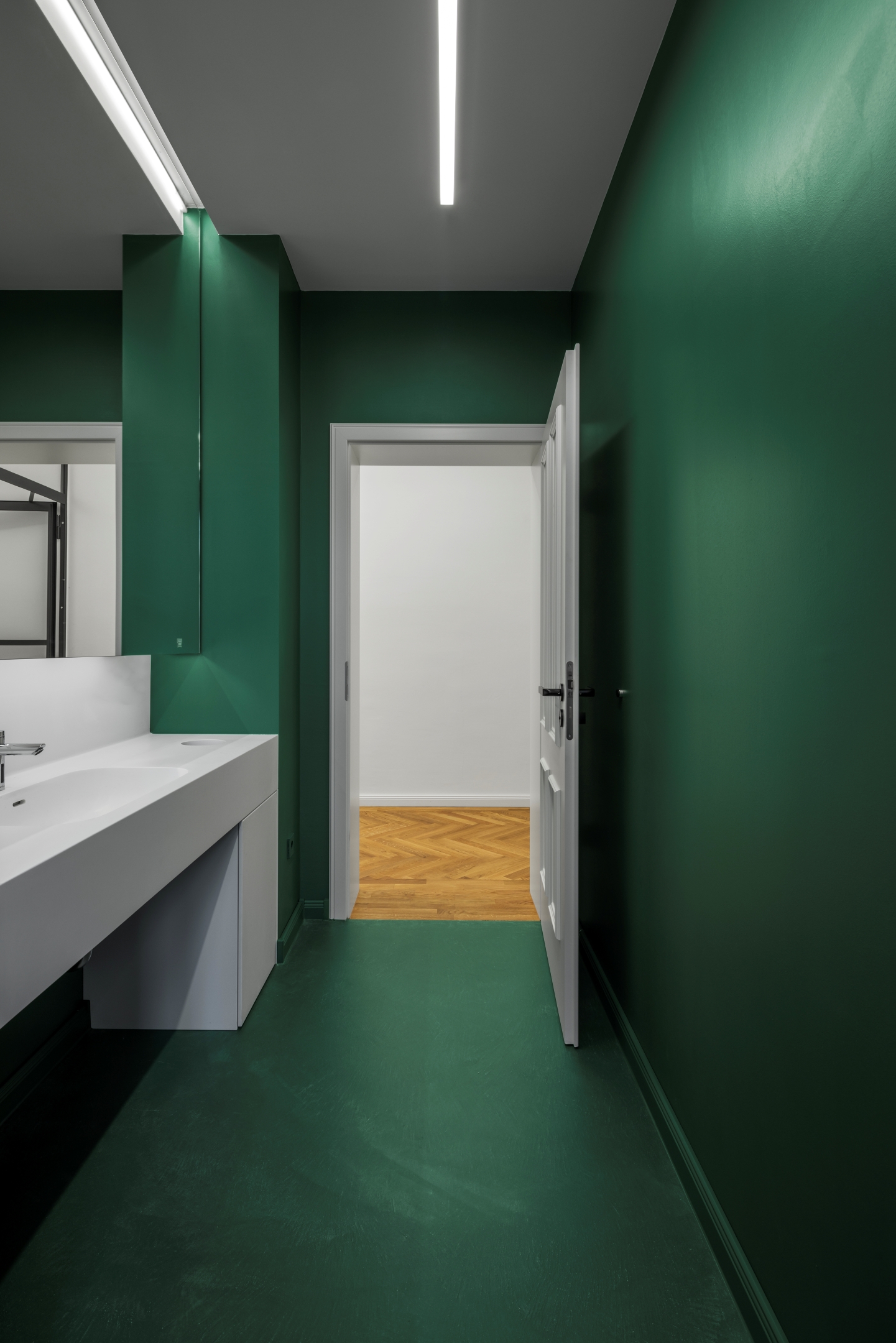 Sanitärbereich im Alten Amtsgericht Furth im Wald mit dunkelgrünem Boden und Wandflächen, Corianwaschtisch, indirekt beleuchtetem Spiegel und verdeckten Spendern.