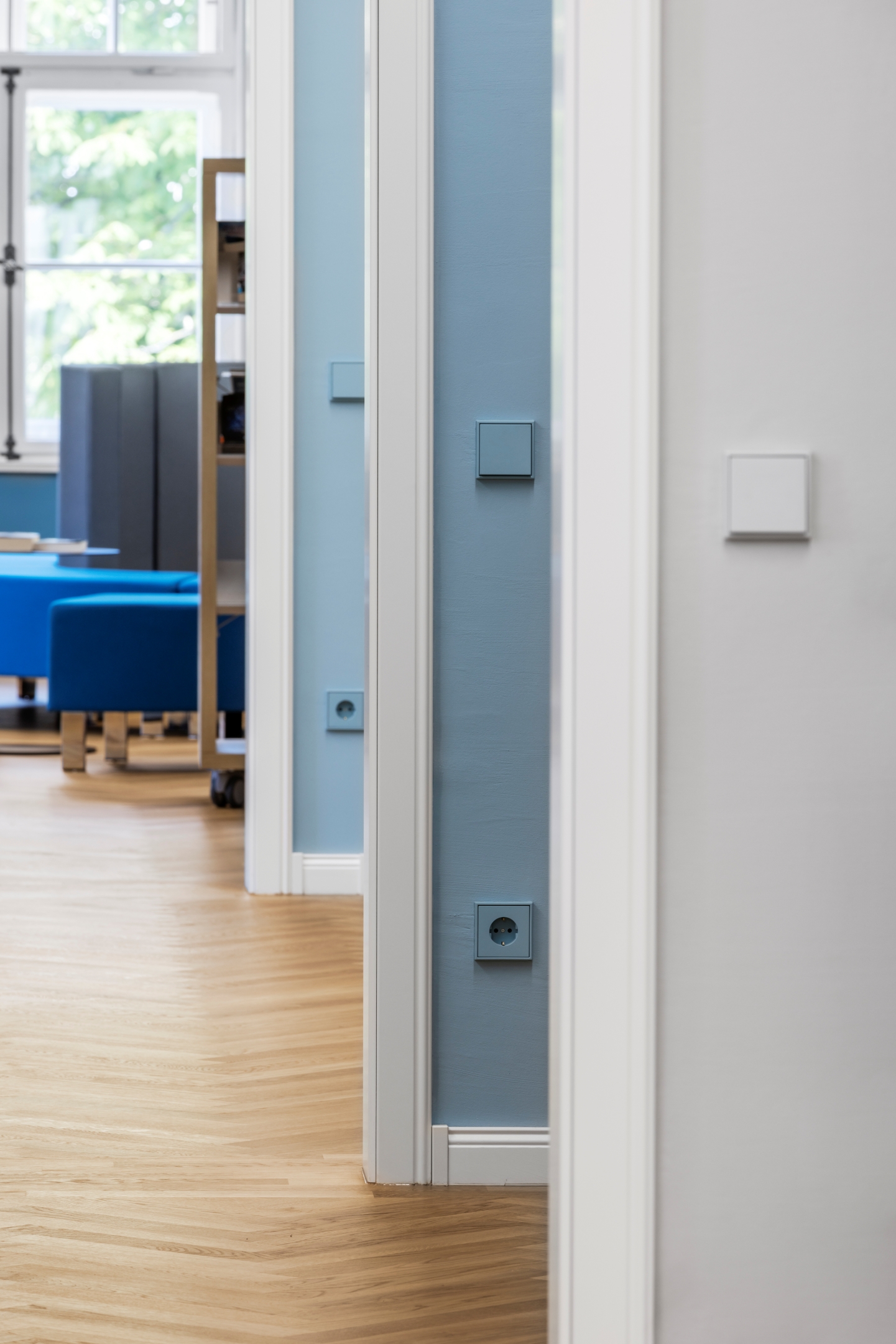 Blick durch mehrere Türleibungen im Alten Amtsgericht Furth im Wald, aufeinanderfolgende Räume in unterschiedlichen Wandfarben Grau, Dunkelblau und Hellblau, jeweils mit farblich abgestimmtem Schalterprogramm von JUNG.
