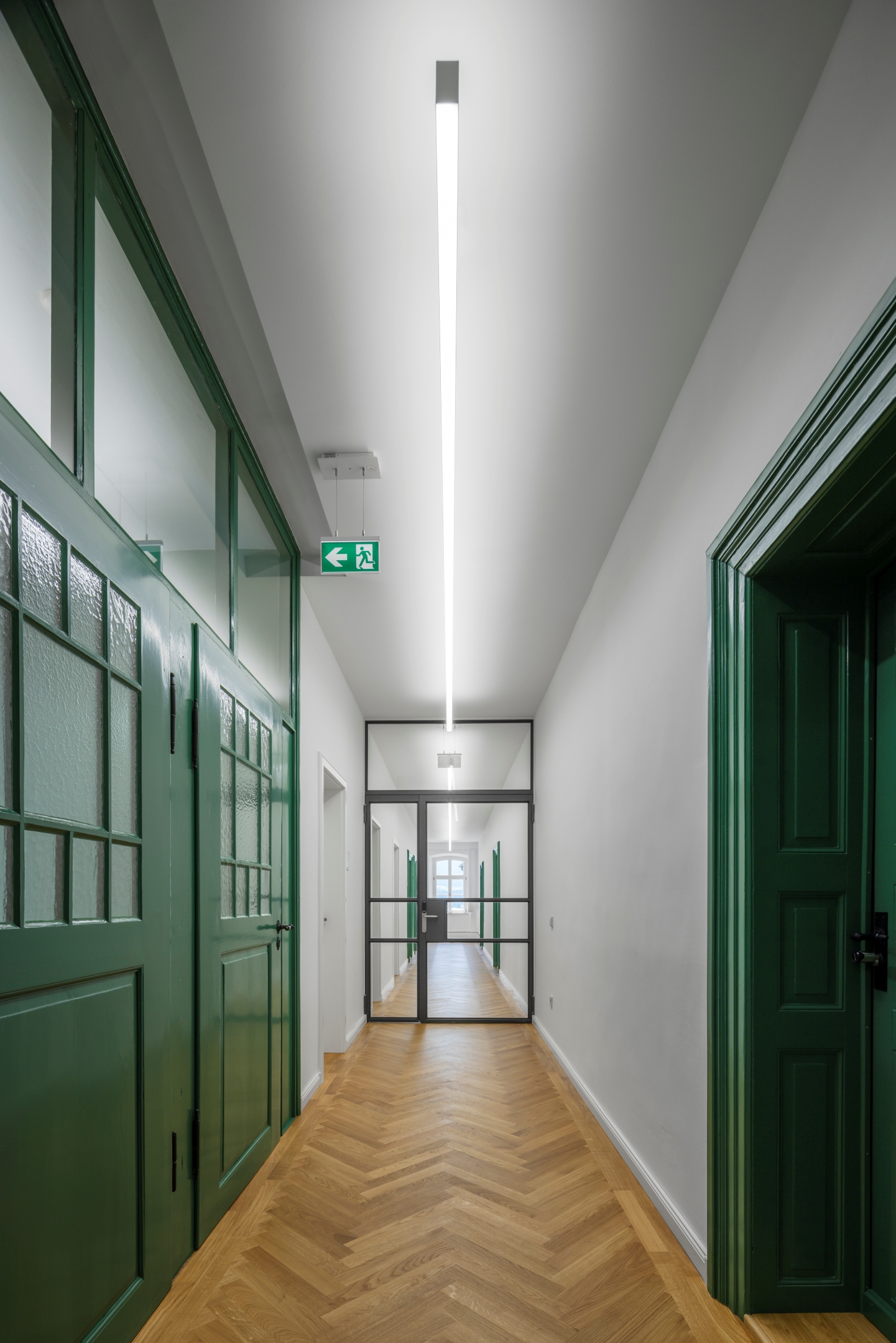 Flur im 2. Obergeschoss des Alten Amtsgerichts Furth im Wald mit Eiche-Parkett, restaurierten historischen Kassettentüren und dunkelgrün gefassten Türrahmen.